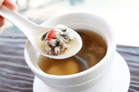 Hand holding the spoon of Chinese cleared soup with black bone chicken and herbs.の写真素材
