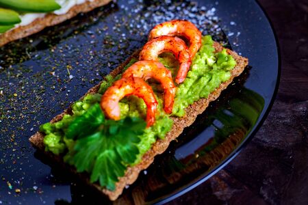 toasted bread with mashed avocado, olives, lemon and peeled fried shrimpの写真素材