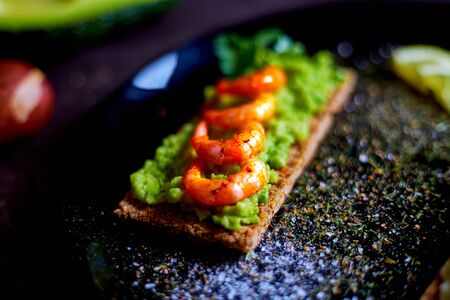 toasted bread with mashed avocado, olives, lemon and peeled fried shrimpの写真素材
