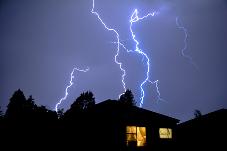 Cloud to Ground Electric Lightning behind house roof tops