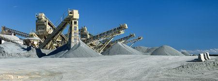 Quarry machines and piles of gravel over blue sky. Stone crushing and screening plant, panoramic...