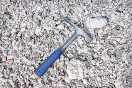 Chisel edge rock pick, geologist exploration tool over natural magnesite rocks background in...