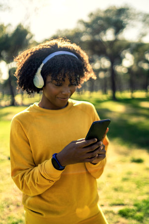 A girl in a yellow tracksuit listening to music in the park with headphones.の写真素材