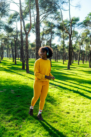 A girl in a yellow tracksuit runs in the park listening to music with blue headphones.の写真素材