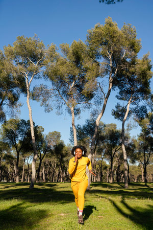 A girl in a yellow tracksuit runs in the park listening to music with blue headphones.の写真素材