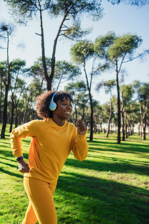A girl in a yellow tracksuit runs in the park listening to music with blue headphones.の写真素材