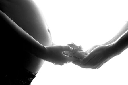 pregnant belly and parents hands holding baby shoesの写真素材