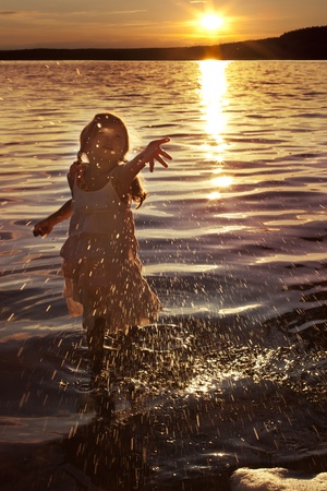little girl splashing water while the sun goes downの写真素材