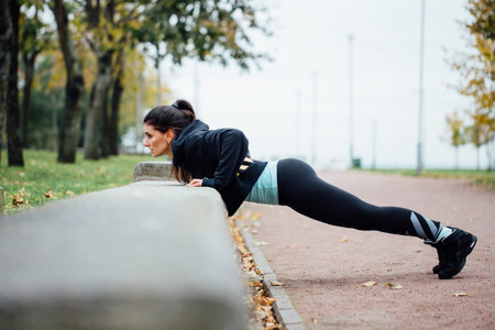 Portrait of woman in sportswear, doing fitness push-ups exercise at fall park, outdoor. Healthy...