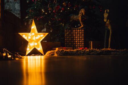 Beautiful Christmas living room with decorated tree, gifts and glowing lights at night. Reflection stars light at floor.の写真素材