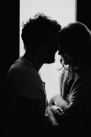 Happy couple of lovers in pajamas having fun and fightingon the windowsill. Christmas atmosphere and new year gift at home. Young family together.の写真素材