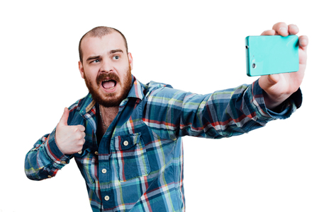 Portrait of a red-bearded, balding male brutal. White isolated background. A man in a blue plaid shirt. Portrait of a happy man taking selfie with thumbs up.Focus on the personの写真素材