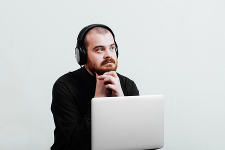 Portrait of a red-bearded, balding male brutal. White isolated background. A man in a black shirt pants. He looks a side  enjoying music on headphonesの写真素材
