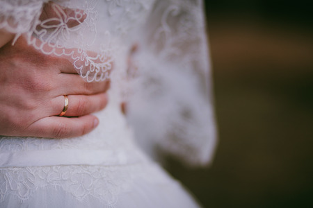 Groom hold bride outdoor. Hand wearing wedding ring on white dress. Close upの写真素材