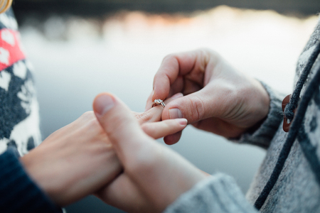 Picture of man putting engagement silver ring on woman hand, outdoor. Seaor river background.の写真素材