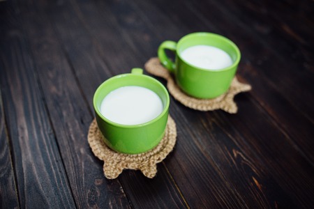 Knitted stand hot dishes and tea cups with , milk. Lying on a background of dark brown wooden planksの写真素材