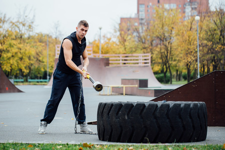 Fitness sport man workout outdoor. with hammer on hands and tractor tire.の写真素材