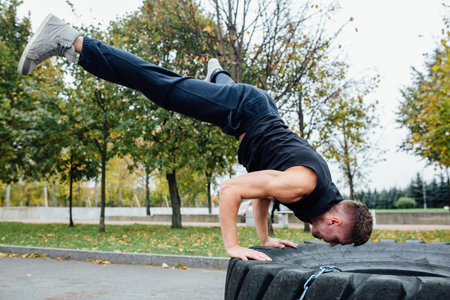 Fitness sport man workout outdoor. with tractor tire in the park. standing on hands.