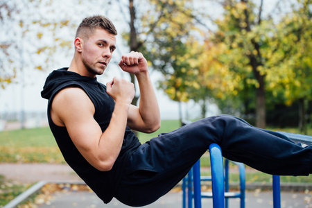 Fitness man doing stomach workouts on parallel bar outdoors. Young attractive man doing abs workout.