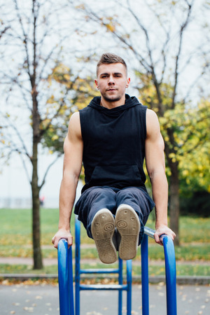 Fitness man doing stomach workouts on parallel bar outdoors. Young attractive man doing abs workout.の写真素材