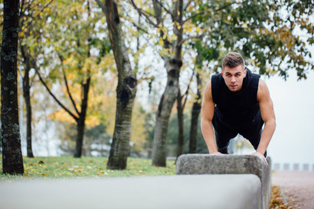 Male runner doing exercise, preparing for morning workout in the fall park. Push ups with bench.