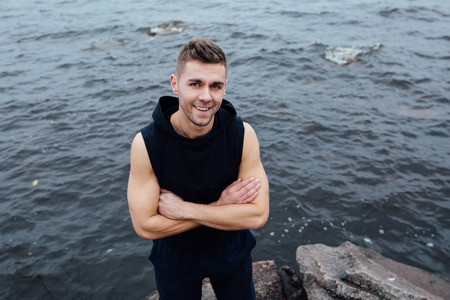 Strong yang fitness man poses on beach near sea and rocks. Fall autumn morning.の写真素材