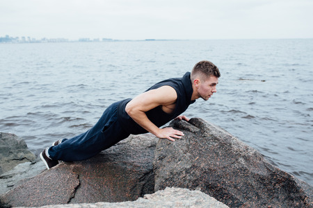 Strong man acts yoga on the rocks beach in the morning against sea. static model posingの写真素材