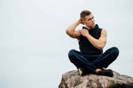 Strong fitness yoga man in lotus pose on the rock beach near the ocean. Harmonic concept, peace and successの写真素材
