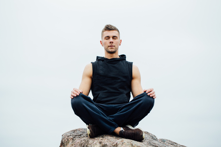 Strong fitness yoga man in lotus pose on the rock beach near the ocean. Harmonic concept, peace and successの写真素材