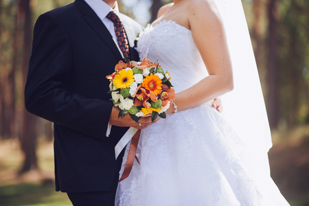 Bride and groom holding wedding bouquet together, outdoor. Love.の写真素材