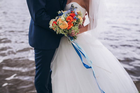 Bride and groom holding wedding bouquet together, outdoor, see oの写真素材