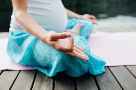 Woman meditating in the lotus position closeup. Hands close-up mudra. Sitting on wooden floor by the riverの写真素材