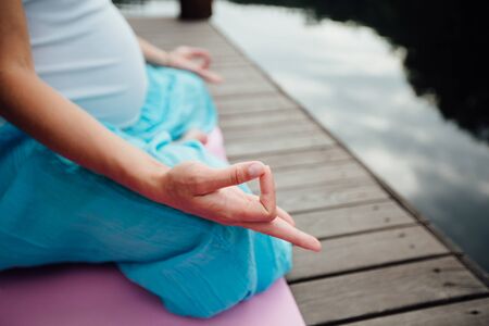 Woman meditating in the lotus position closeup. Hands close-up mudra. Sitting on wooden floor by the riverの写真素材