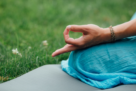 Woman meditating in lotus position closeup. Hands close-up mudra. Sitting on rug the lawn of green grass backgroundの写真素材