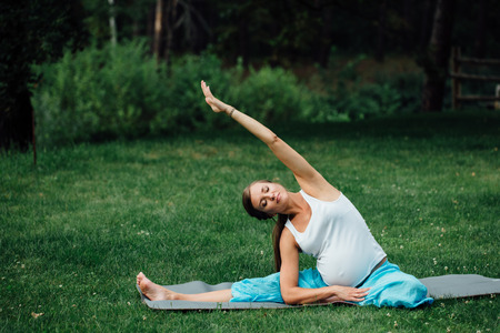 pregnant yoga in the lotus position on the forest background. in the park the grass mat, outdoor, health woman.の写真素材