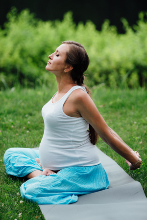 pregnant yoga in the lotus position on the forest background. in the park the grass mat, outdoor, health woman.の写真素材