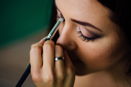 Make-up artist hand applying bright base color on models face and holding a brush , close .の写真素材