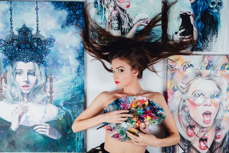 Beautiful female Nude artist surrounded by paintings canvas on the floor white background. brushes and palette.の写真素材