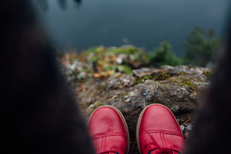 Creative girl standing on the edge of a picturesque cliff. Tourist in jeans and red boots hipster sneakers.の写真素材