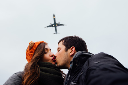 A guy and a girl, the couple embraced doing selfie standing in a picturesque place rocks. Against the background of a plane flies overhead. Autumn sky. Brunette long hair, knitted bandage.の写真素材