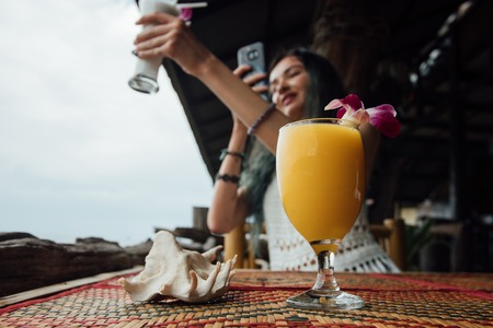 Orange mango juice in a glass with a flower next to a sea shell In the foreground.の写真素材