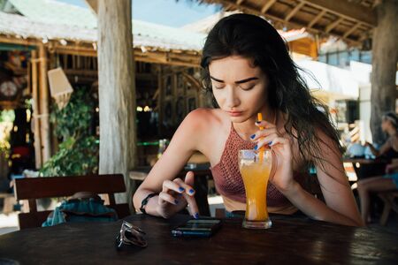 girl drinks juice and checks the phone cafe on vacation with a view of the sea and the beach.の写真素材