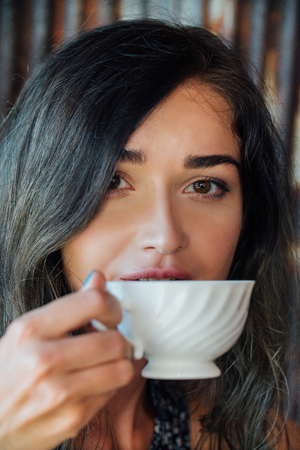 Portrait of a girl drinking coffee in a vintage cafe on the terrace in Asia. Sniffs, drinks.の写真素材