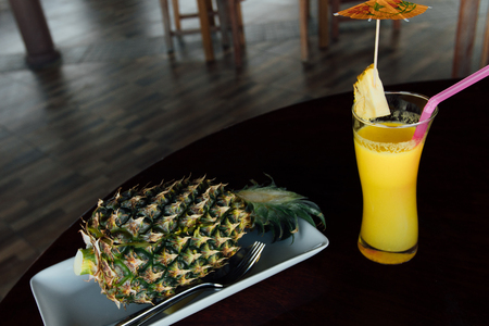 Fried rice inside pineapple next to a glass of juice with a straw and slices of fruit.の写真素材