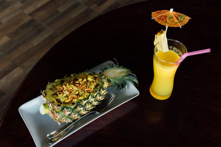 Fried rice inside pineapple next to a glass of juice with a straw and slices of fruit.の写真素材