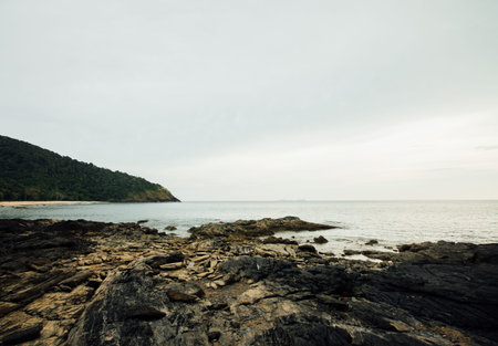 Rocky sea shore against a cloudy sky. Green hill on background cloudy sky