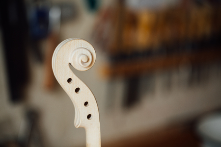 Wooden detail of the head of the violin. Raw wood, texture. Against the background of workshop.の写真素材