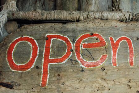 Text sign is open on a wooden board. Close up sign open on wooden background. Text on wooden texture open. Written red letters text open on signboardの写真素材