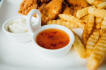 French fries, chicken nuggets and sauces on a white plateの写真素材