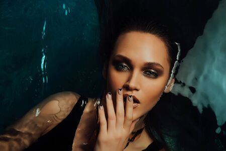 Portrait of beautiful hot woman lies on the water pool. Fingers touch the lips sexually.の写真素材